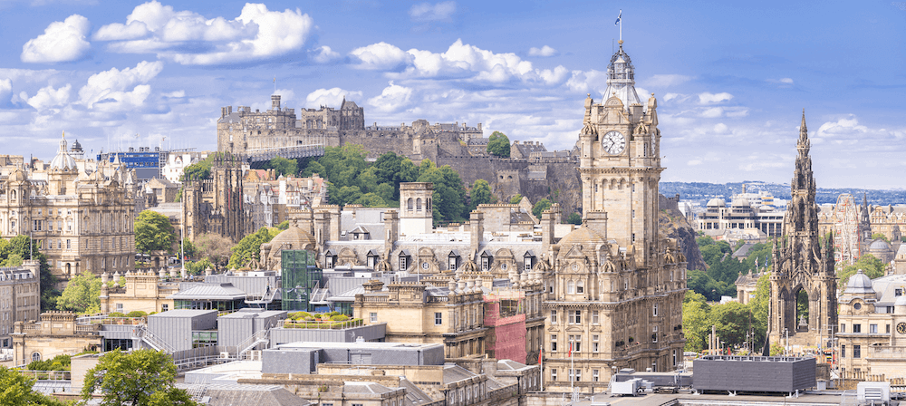 A view from Calton Hill of one of the best cities to visit in Scotland: the capital city of Edinburgh. Image shows the Edinburgh cityscape, with Edinburgh Castle in the background