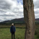 A person beside a towering standing stone on a trip to Scotland