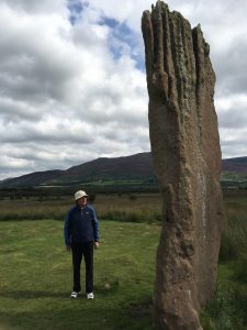 A person beside a towering standing stone on a trip to Scotland